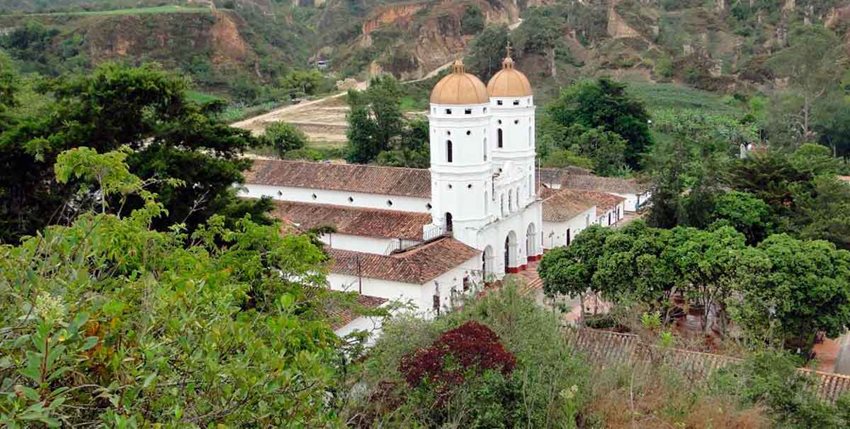 Panorámica de iglesia blanca, con dos torres, en medio de árboles.